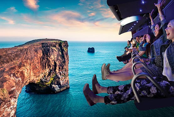 Riders on a flight ride over a rocky cliffside by the ocean.