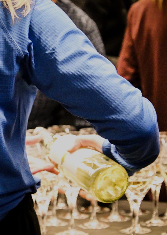 A person pours white wine into an array of glasses.