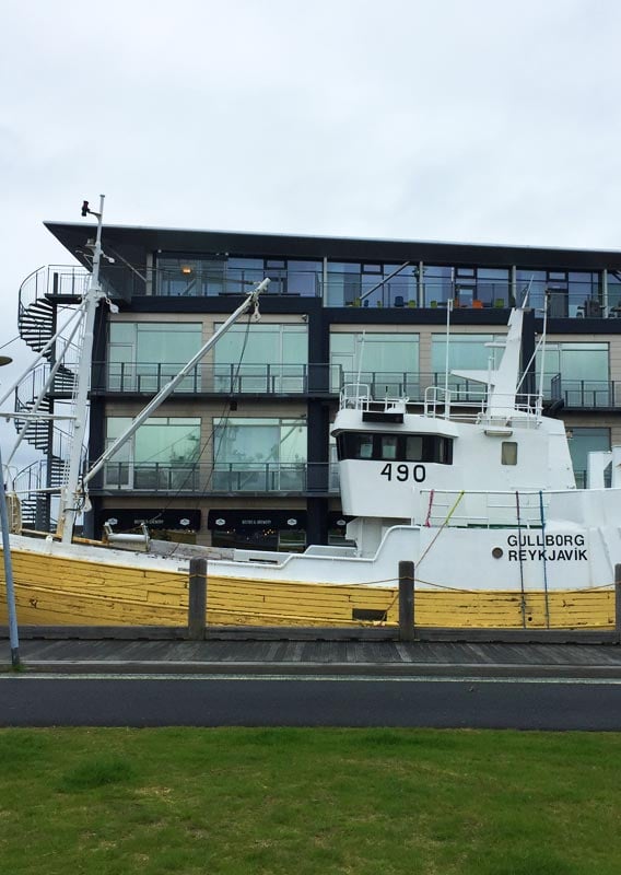 A yellow and white boat sat in a harbour next to a glass building