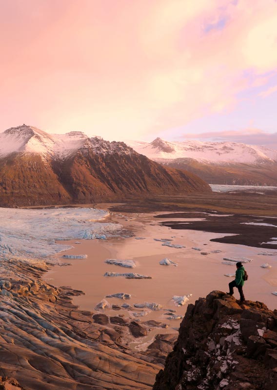 Hiker stands above calving glacier and mountain view at sunset