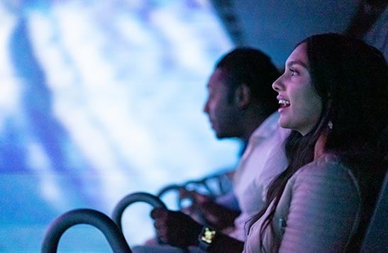 People sitting on a flight ride in front of a glowing screen.