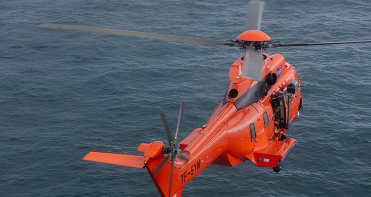 An orange helicopter flies over the open ocean.